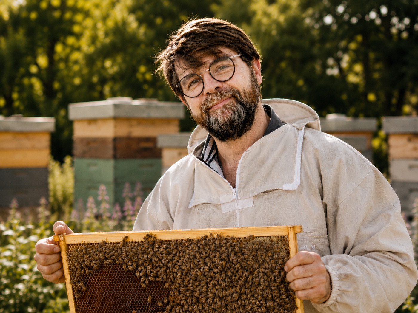 Robin Dussauchoy, apiculteur à Grandris, souriant en vareuse devant ses ruches, un cadre de ruche couvert d’abeilles entre les mains